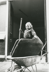 862434 Afbeelding van Alexander Huiding in een kruiwagen voor de deur van de voormalige Waterstraatschool (Waterstraat ...